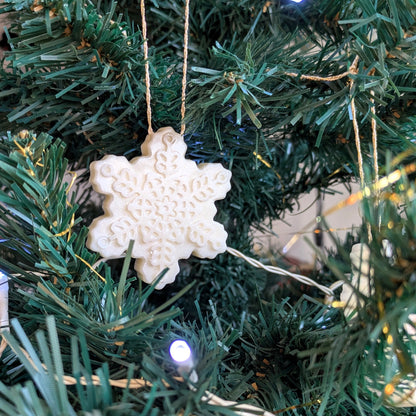 White snowflake ornamelt hanging on a green Christmas tree with lights.