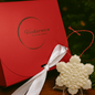 White snowflake-shaped ornament with a red box featuring 'Voskarnica' branding on a Christmas tree background.