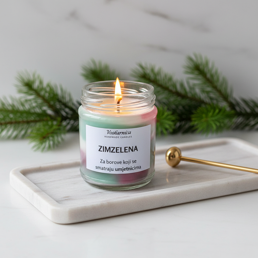 Candle in a glass jar labeled 'Zimzelena' on a marble tray with greenery in the background